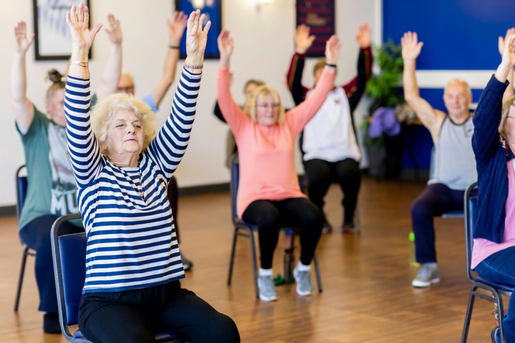 Group of senior adults participating in a chair exercise class, promoting fitness and healthy lifestyle.