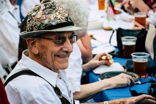 Smiling elderly man in festive attire and hat enjoying Oktoberfest with friends.