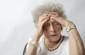 An elderly woman with her hands on her head, appearing stressed or in pain.