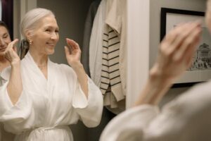 Senior woman in bathrobe smiling at her reflection in the bathroom mirror