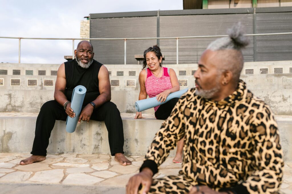 Group of adults preparing for an outdoor yoga class with mats in hand, promoting wellness and fitness.