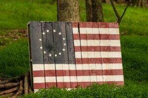 A painted wooden Betsy Ross flag placed outdoors against a tree.