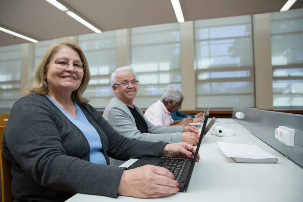Smiling seniors learning computer skills in a modern classroom setting.