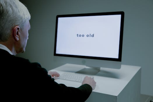 Senior man at computer facing ageism online, "too old" displayed on screen.