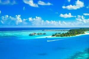 Aerial view of a luxurious tropical resort on a pristine island surrounded by azure waters and lush greenery.