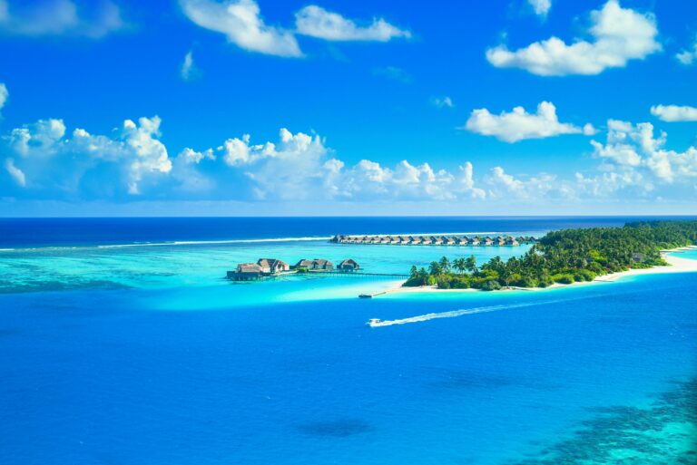 Aerial view of a luxurious tropical resort on a pristine island surrounded by azure waters and lush greenery.