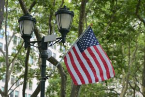 A street lamp with an American flag in New York City surrounded by green trees.