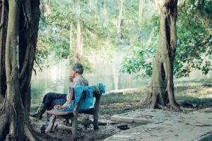 Senior man relaxing and smoking on a bench in a tranquil Hanoi park.