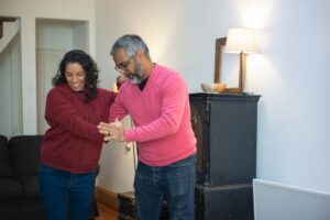 Happy couple dancing together at home, enjoying a joyful moment indoors with warm lighting.