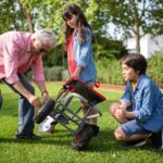 An elderly man assists two children in fixing a garden cart outdoors, showcasing family bonding and teamwork.