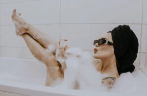 A woman enjoying a relaxing bubble bath with wine, sunglasses, and a towel turban.