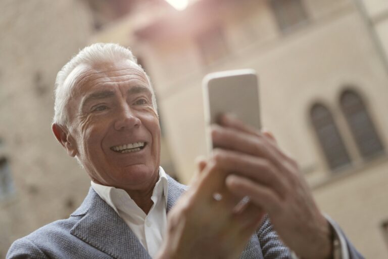 Elderly man smiling while video calling on a smartphone outdoors.