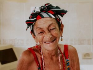 Smiling elderly woman with a vibrant headscarf and beaded necklace indoors.