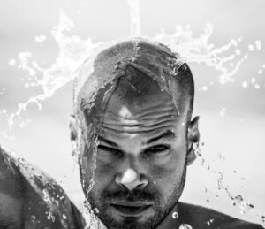 Dramatic black and white portrait of a man splashing water on his face in a studio setting.