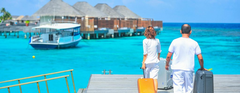 A couple arriving at a luxurious Maldives resort dock with luggage, capturing a tropical vacation vibe.