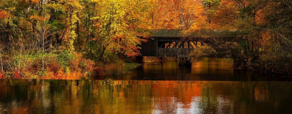 Beautiful autumn landscape with a covered bridge and vibrant fall foliage reflecting on a calm river.