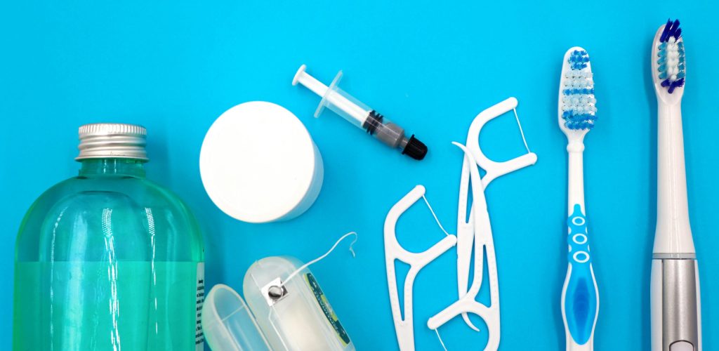 Flat lay of oral hygiene essentials including toothbrushes, floss, and mouthwash on a blue surface.