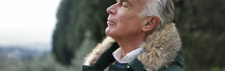 Senior man with white hair, eyes closed enjoying fresh air in Tuscany's natural setting.