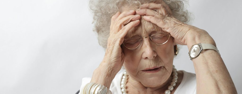 An elderly woman with her hands on her head, appearing stressed or in pain.