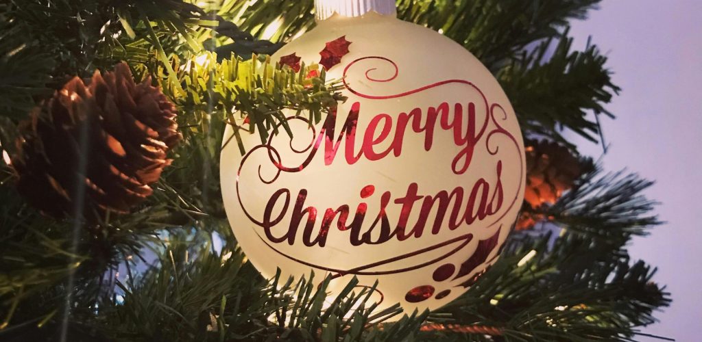 Close-up of a 'Merry Christmas' ornament on a decorated tree with lights.