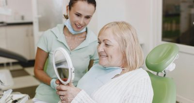 Senior woman smiles while checking her teeth in a mirror with a dentist. Healthcare and dentistry concept.