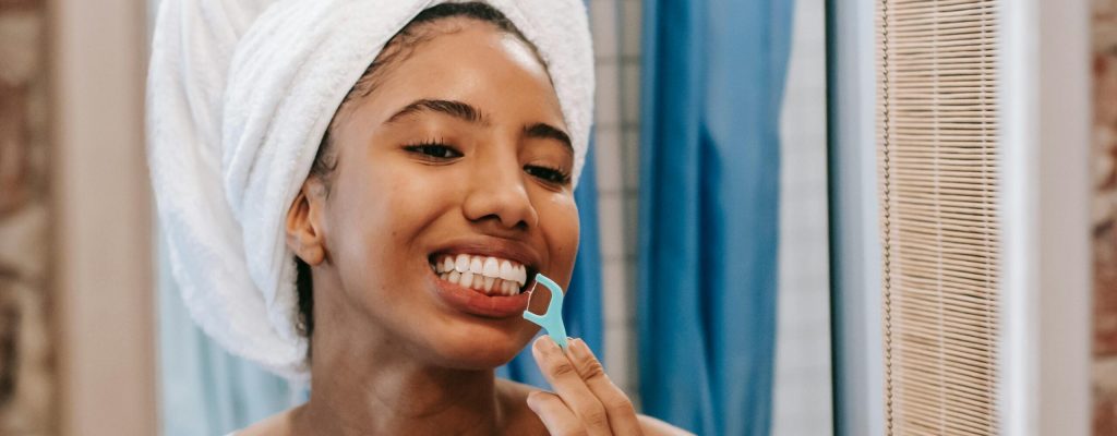 pexels-photo-5938291-5938291 Young woman with towel on head flossing teeth in bathroom mirror, promoting hygiene and wellness.