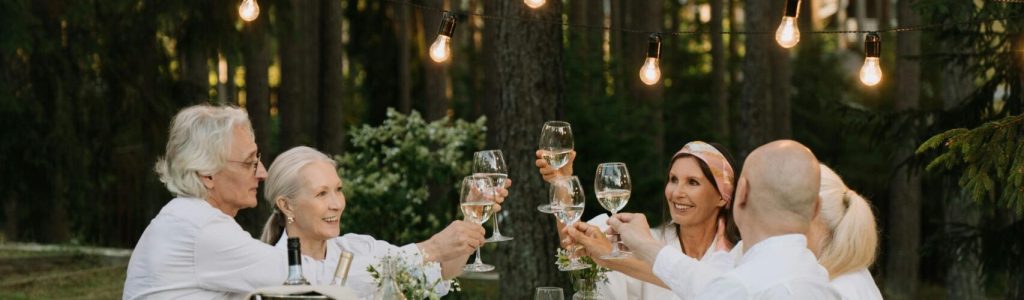 A group of friends toasting in a cheerful outdoor dinner setting surrounded by nature.