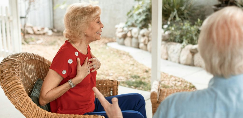 Senior woman in red shirt smiling and conversing in a garden setting.
