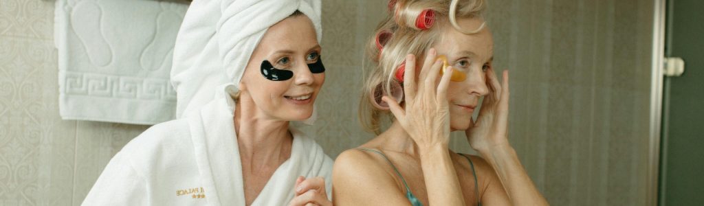 Two women enjoying a beauty routine with face masks and hair rollers.