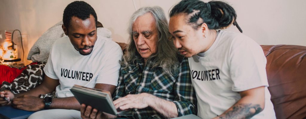 Volunteers helping an elderly man review a photo album during a home visit, fostering community support.