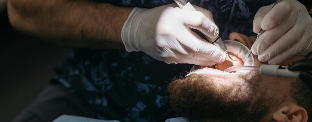 Dentist using tools for dental examination on a bearded male patient.