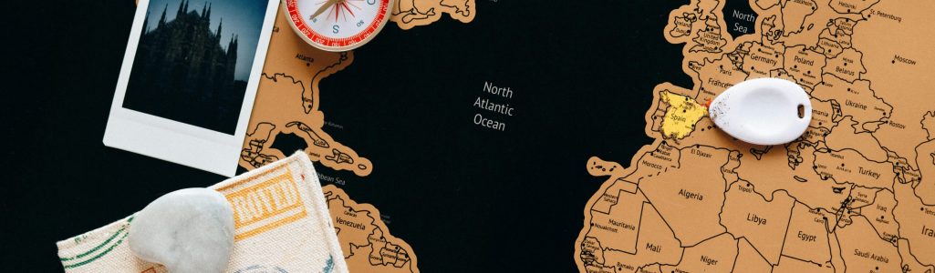 Flat lay of travel items including a map, compass, and polaroid for adventure planning.