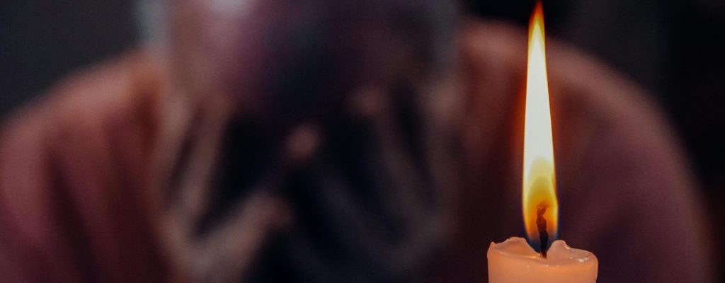 A senior adult in an emotional moment lit by a candle, symbolizing reflection and grief.