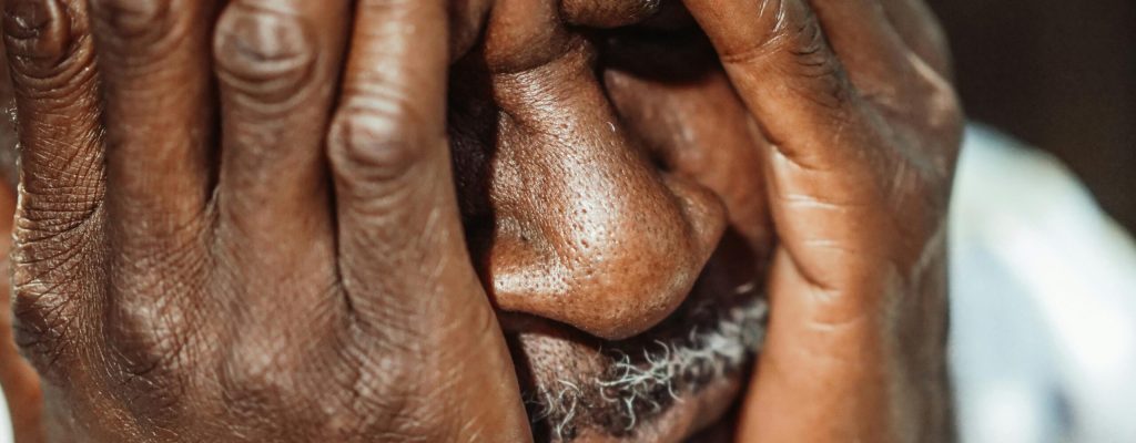 Close-up portrait of an elderly man with hands covering face, showing emotion.