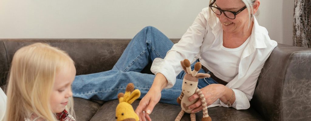 A grandmother and granddaughter having fun with knitted toys on a sofa, showcasing family bonding moments.