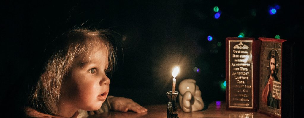 A young girl gazes in awe at a candlelight, surrounded by a serene, dark ambiance.